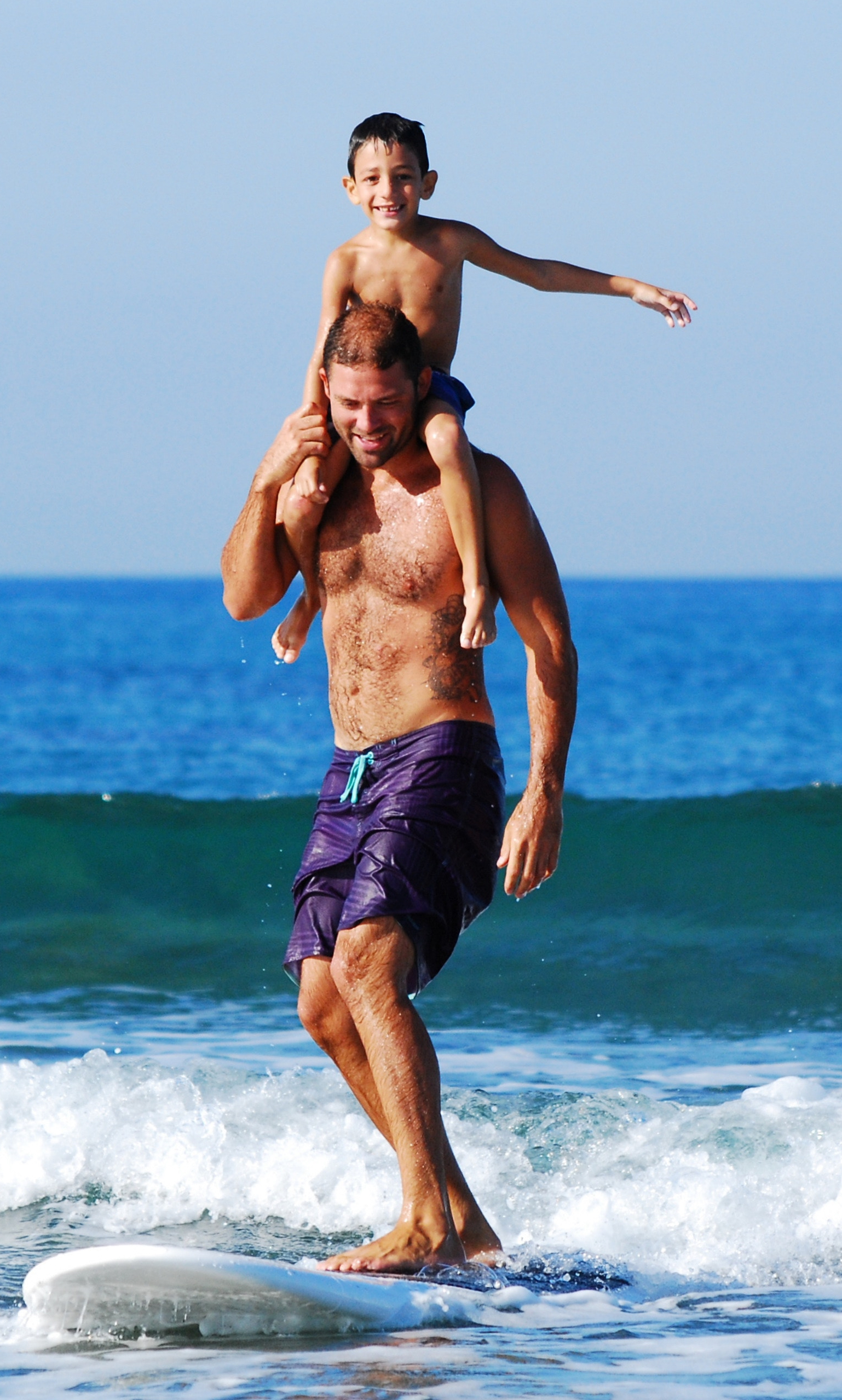 Père surfe avec fils sur le dos