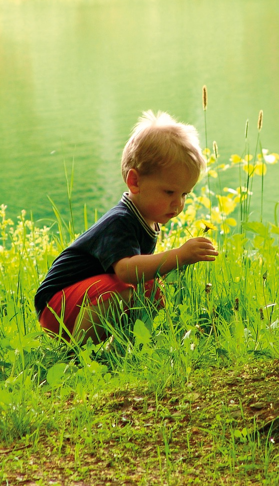 Un garçon accroupi dans l'herbe près d'une rivière Garçon accroupi près d'une rivière